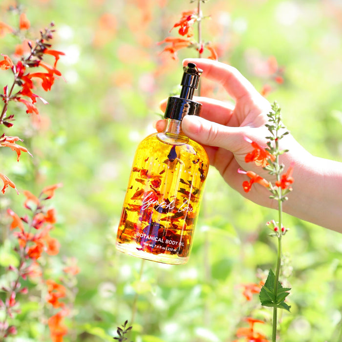 Hand holding botanical body oil among flowers