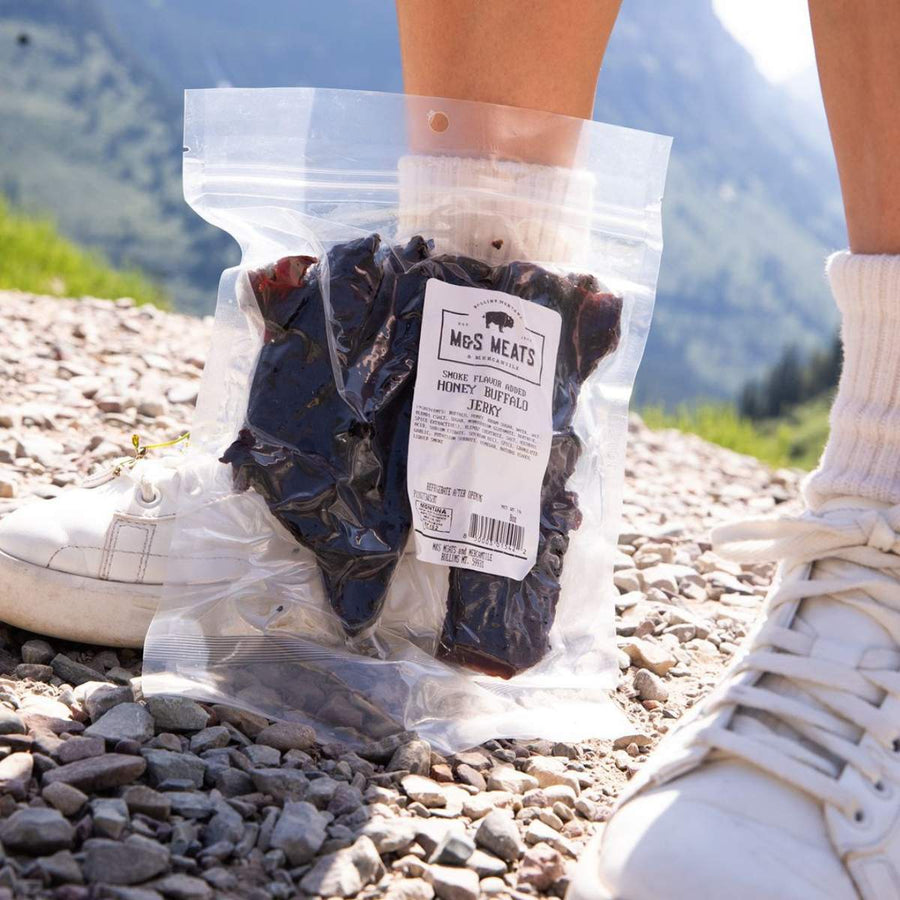 Honey Buffalo Jerky, package held beside hiking shoes outdoors
