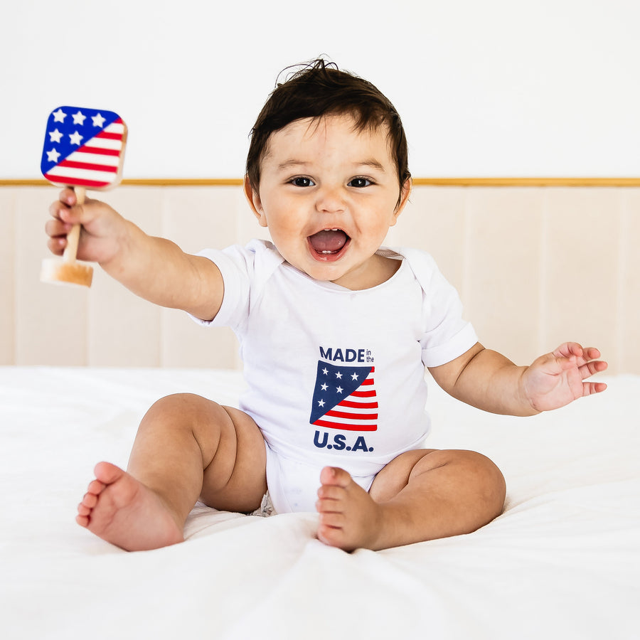 Baby holding an American flag-shaped wooden rattle