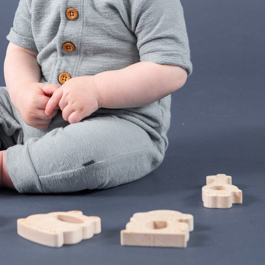 Baby holding a wooden cross-shaped rattle beside other wooden toys