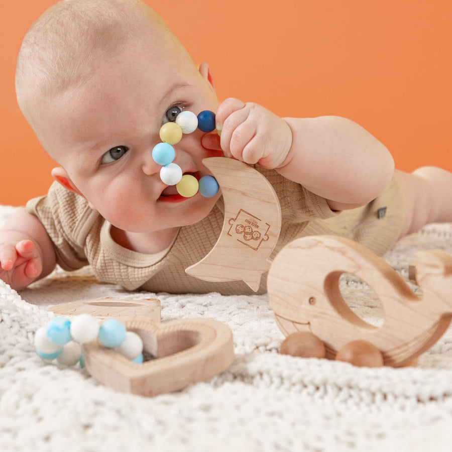 Baby holding a wooden teether with silicone beads during supervised play
