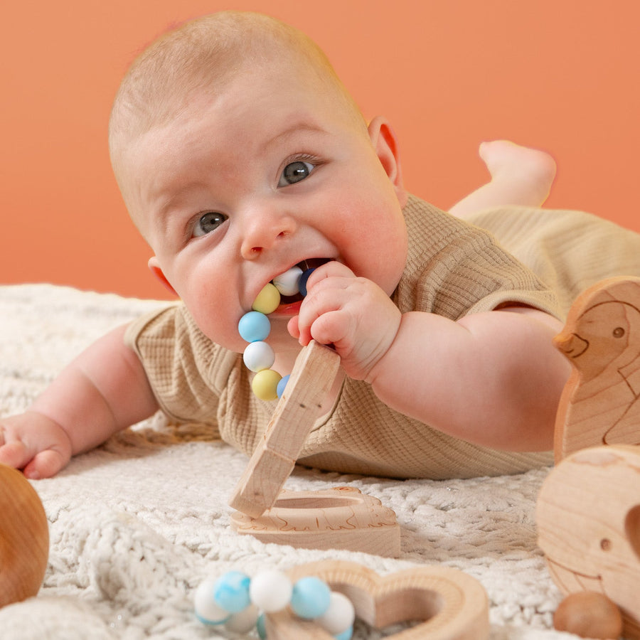 Baby holding a wooden teether with silicone beads during supervised play