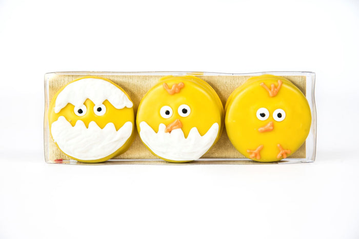 Three chocolate-dipped Oreo cookies decorated as hatching Easter chicks in a clear box