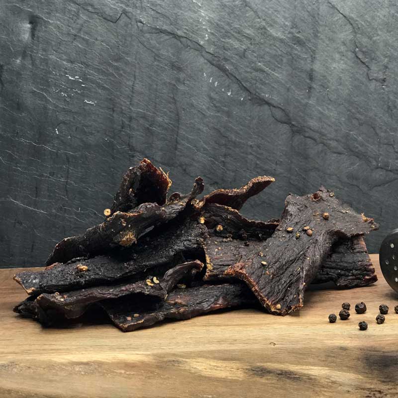 Pepper Buffalo Jerky, dried strips and peppercorns on a board