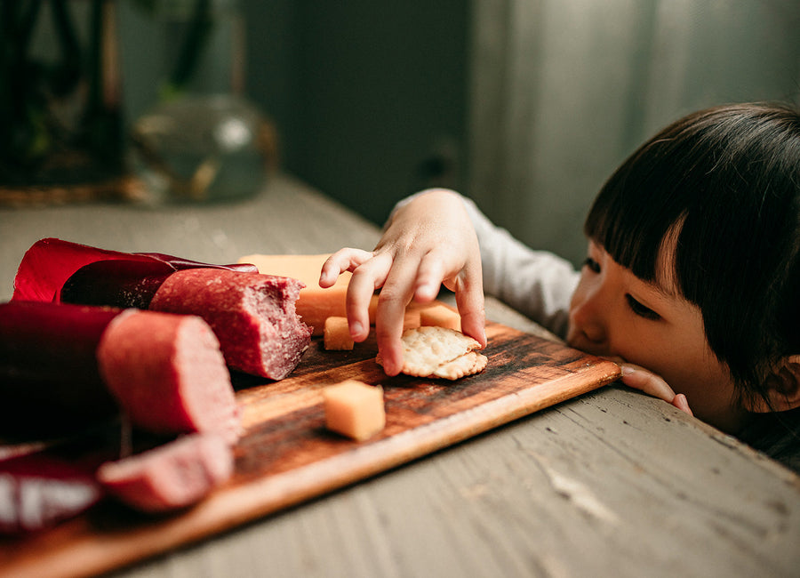Person reaching for sliced sausage on a wooden board; serving suggestion