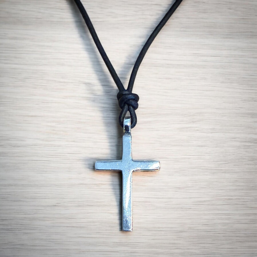 Classic cross on black leather cord against pale wood