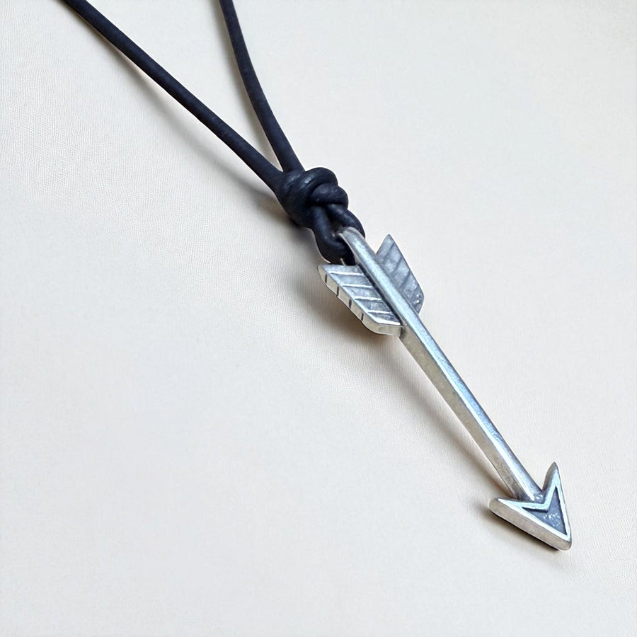 Arrow pendant on black leather cord against a light background