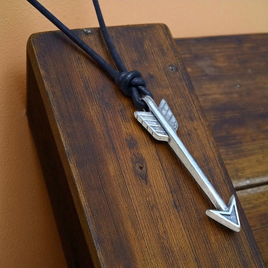 Arrow pendant on black leather cord on wood