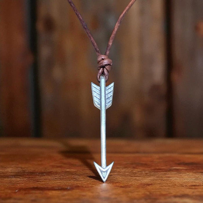 Arrow pendant on brown leather cord against wood