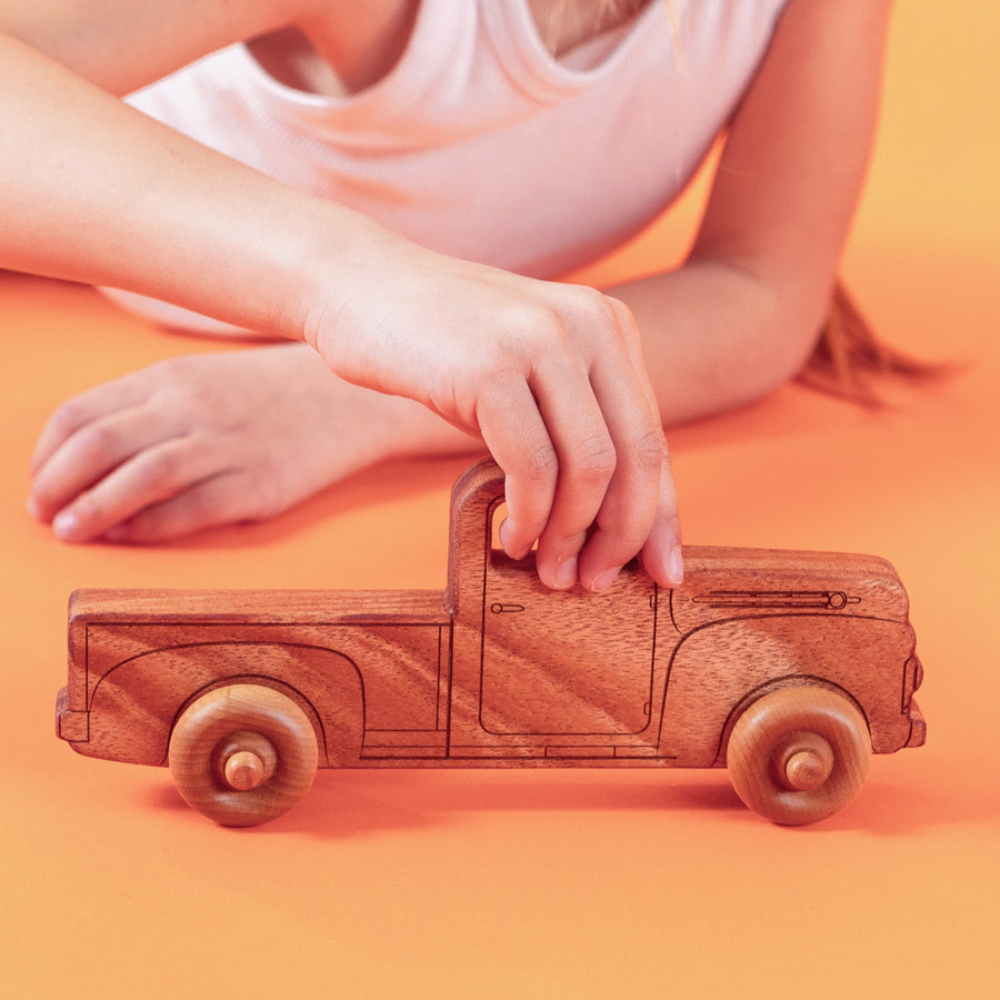 Child’s hands pushing a natural wood toy pickup truck