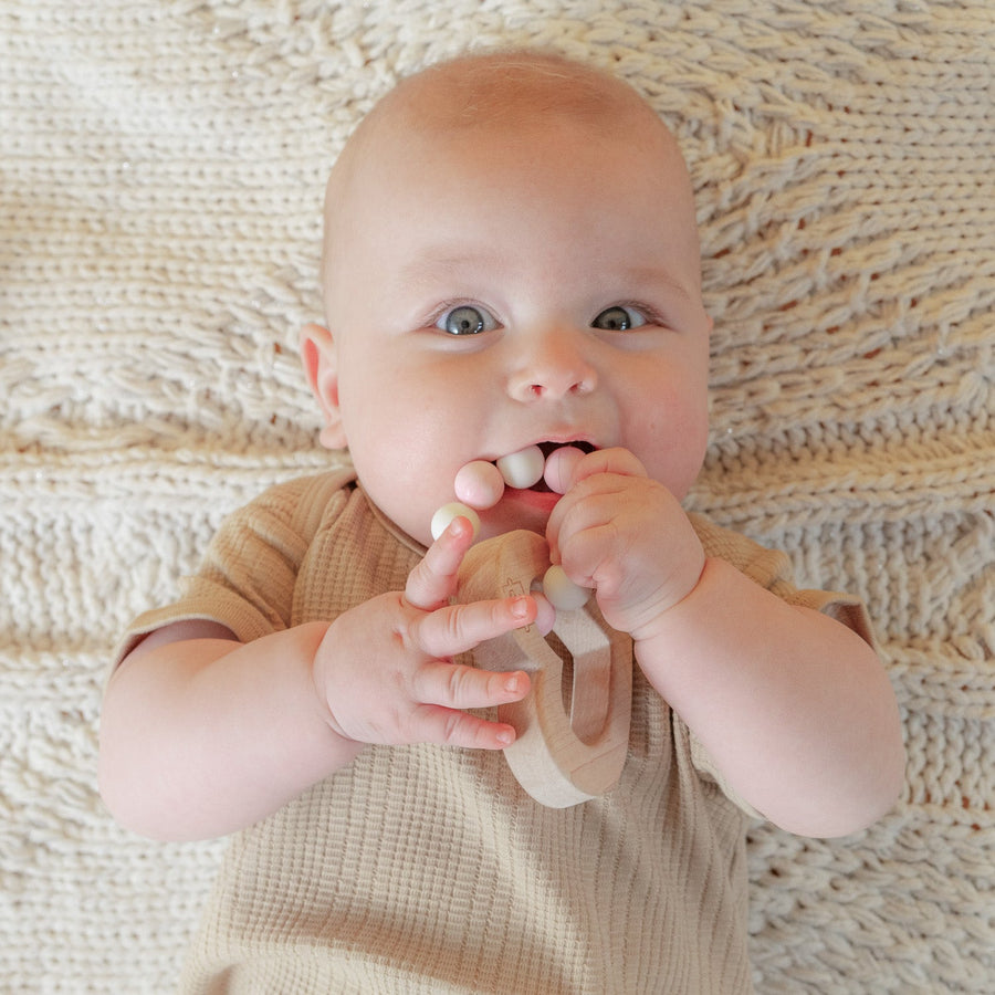 Baby holding a wooden teether with silicone beads during supervised play