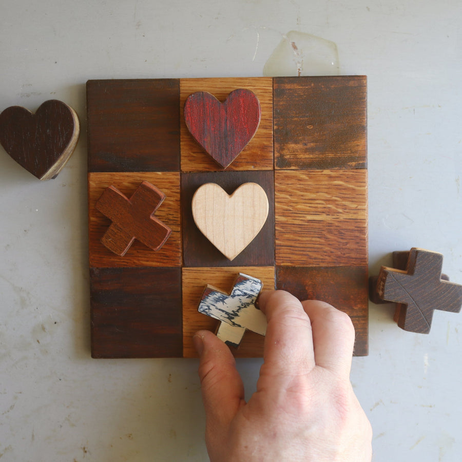 Wooden tic-tac-toe board with heart and X playing pieces.