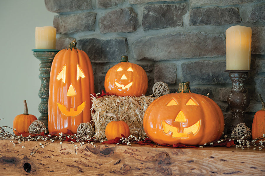 Illuminated stoneware jack-o-lantern pumpkins in a seasonal display; coordinating pieces are separate