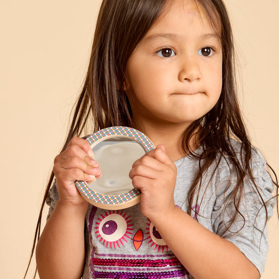 Child holding a round wooden-framed discovery mirror