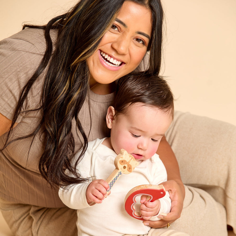 Baby holding a bird-shaped wooden rattle and teether