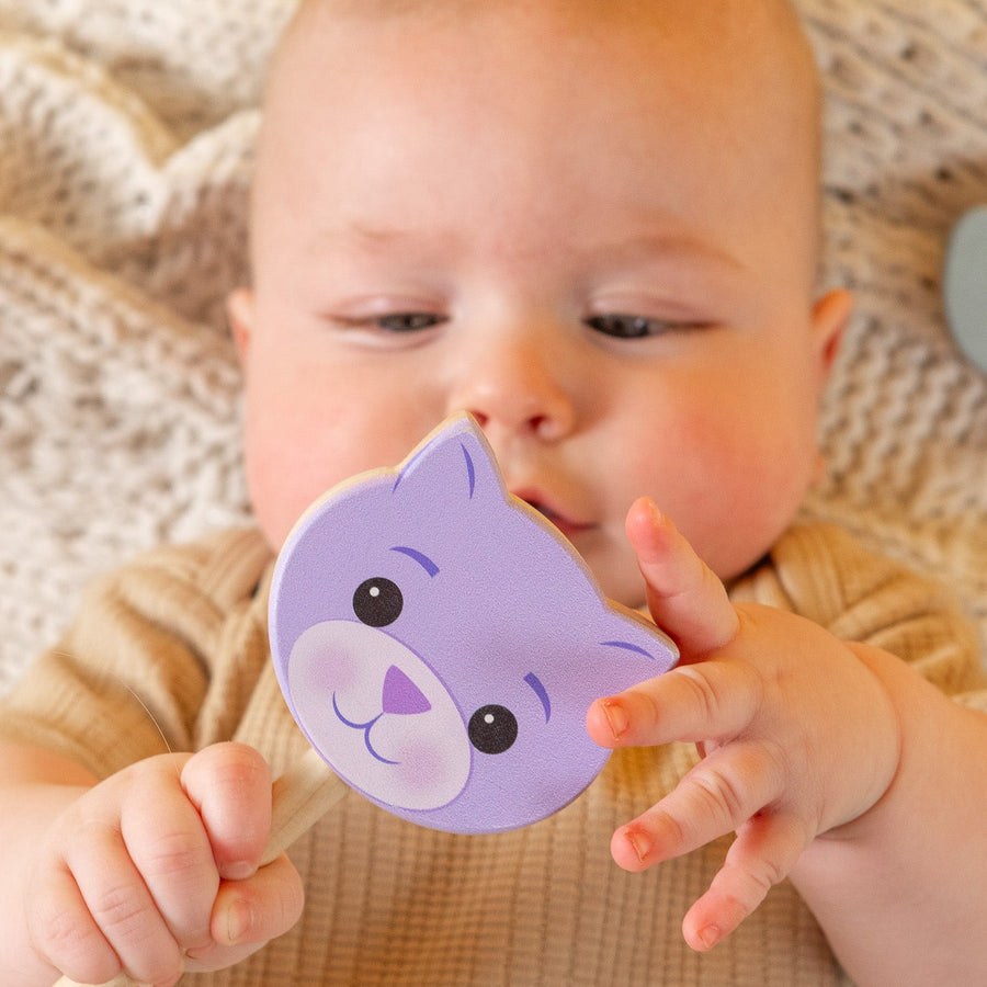 Baby holding a purple cat-shaped wooden rattle