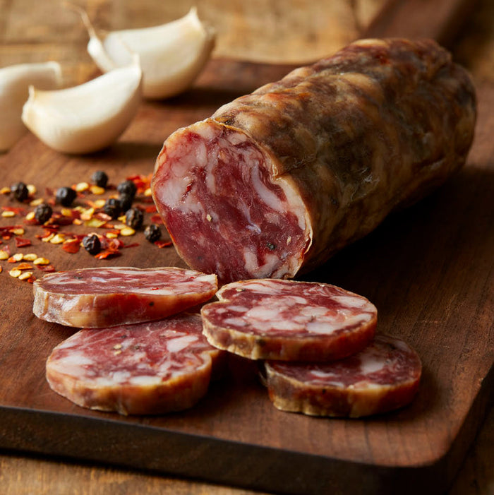 Red Wine & Garlic salami sliced on a wooden board with garlic cloves and pepper flakes.