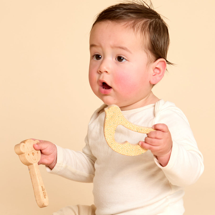 Baby holding a wooden animal-shaped rattle during supervised play
