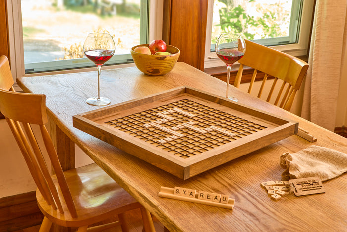 Rotating wooden Scrabble board with letter holders and tile bag on a dining table