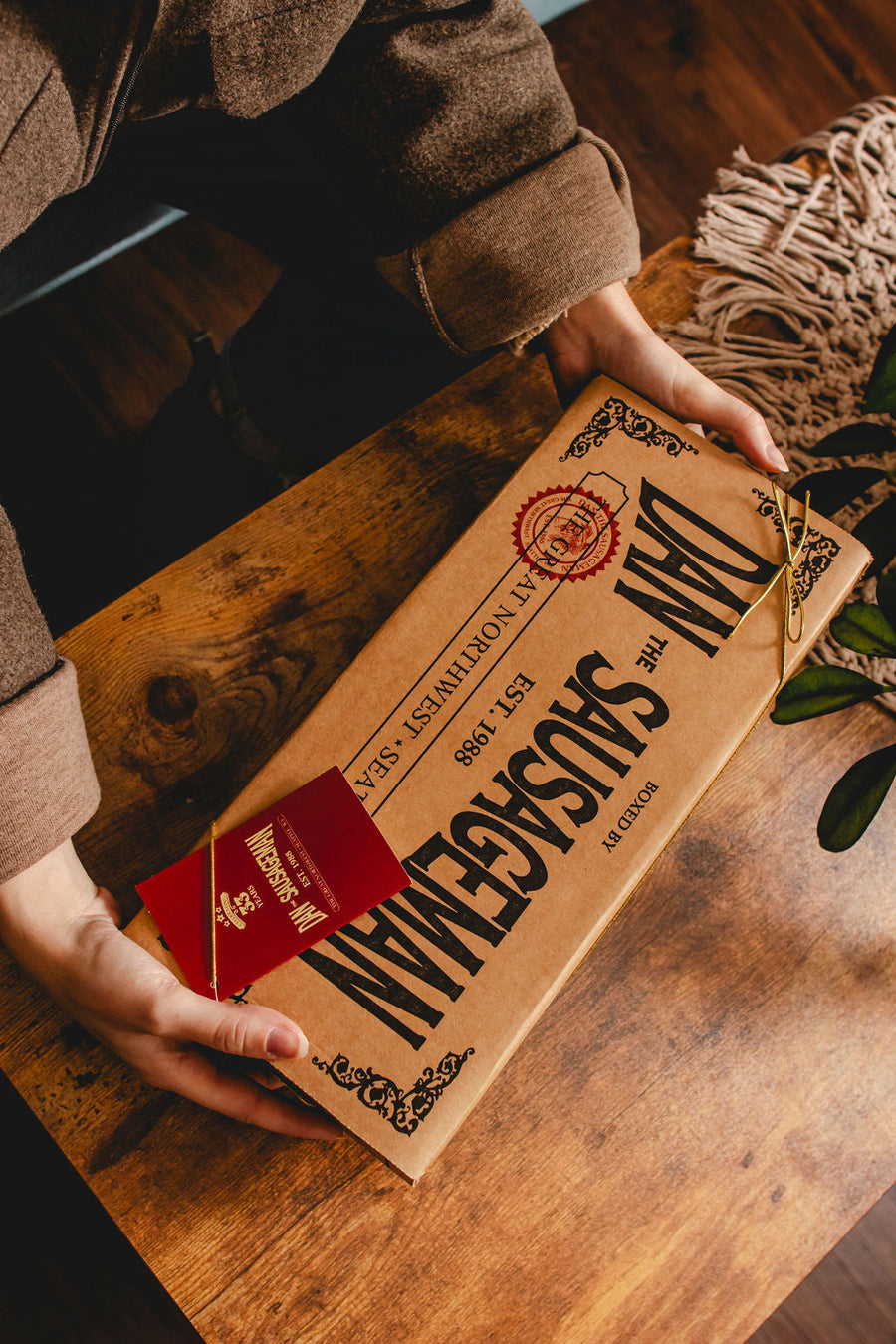 Hands holding a closed Dan The Sausageman gift box with red tag