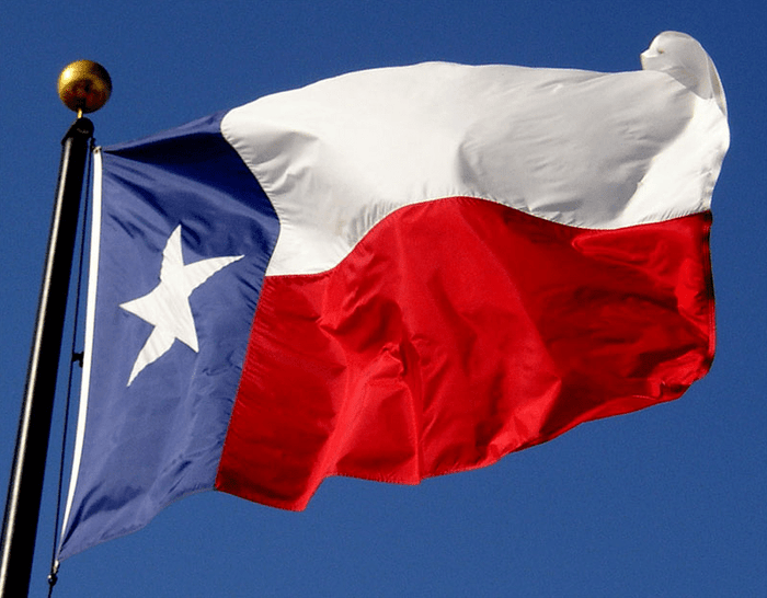 Texas state flag flying from an outdoor flagpole against a blue sky