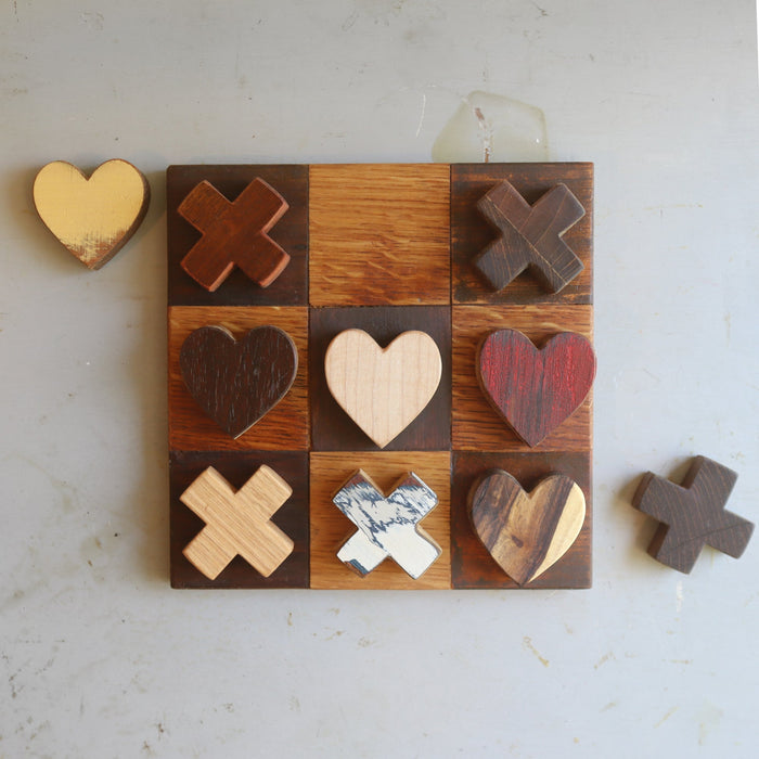 Wooden tic-tac-toe board with heart and X playing pieces.