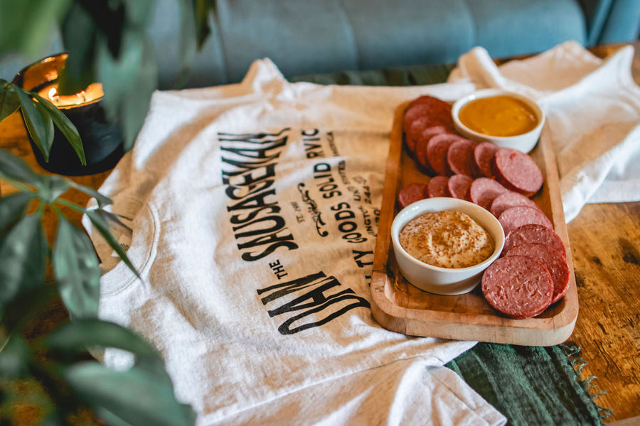 Sliced sausage, crackers and mustard on a small wooden board beside printed wrapping; serving suggestion