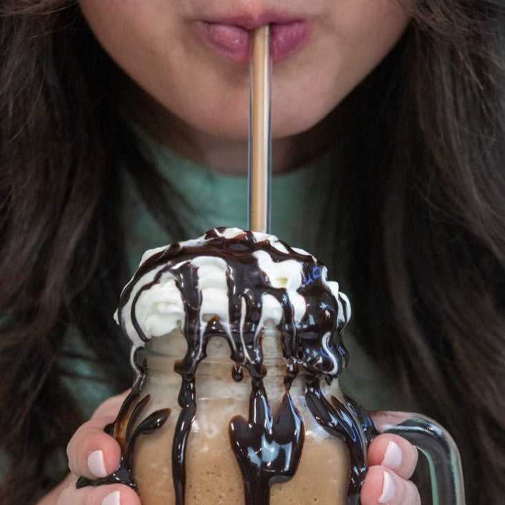 Person sipping a frozen hot chocolate topped with whipped topping and chocolate