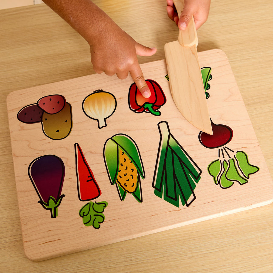 Child using a wooden knife and illustrated cutting board during food preparation