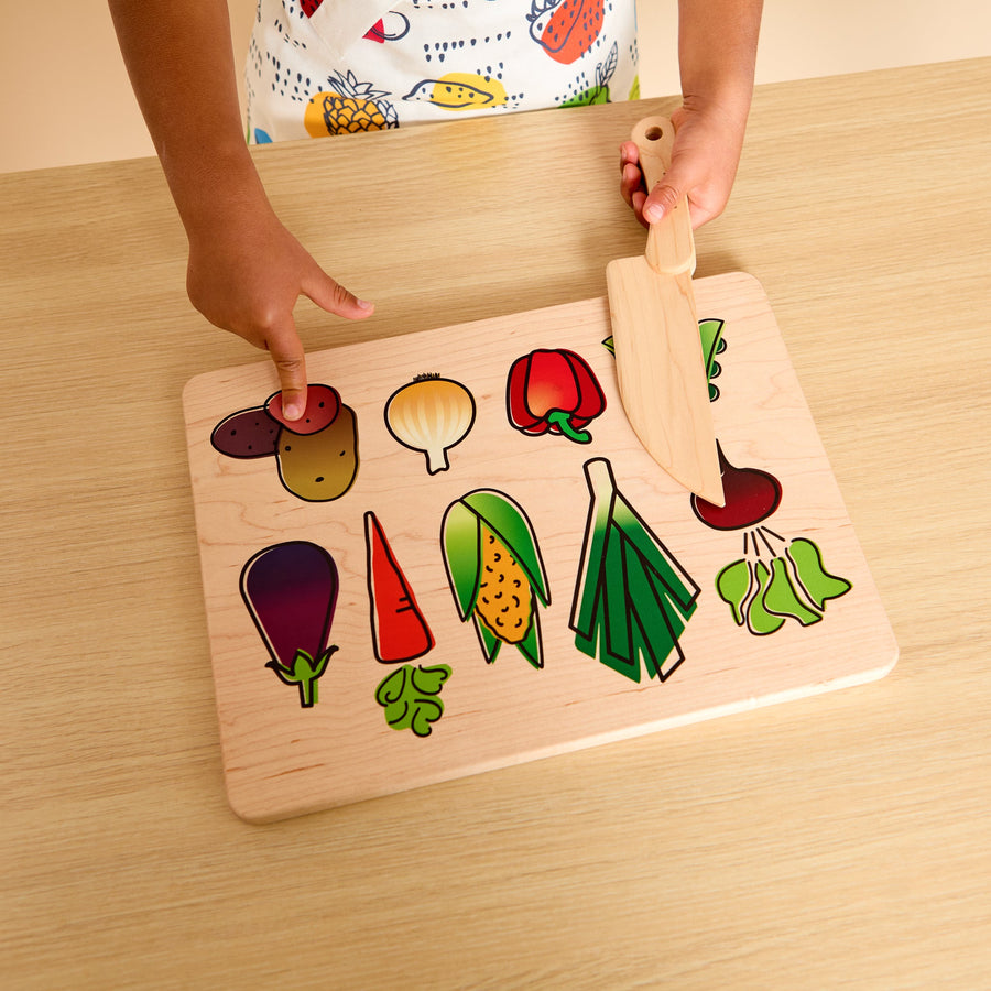 Child using a wooden knife and illustrated cutting board during food preparation
