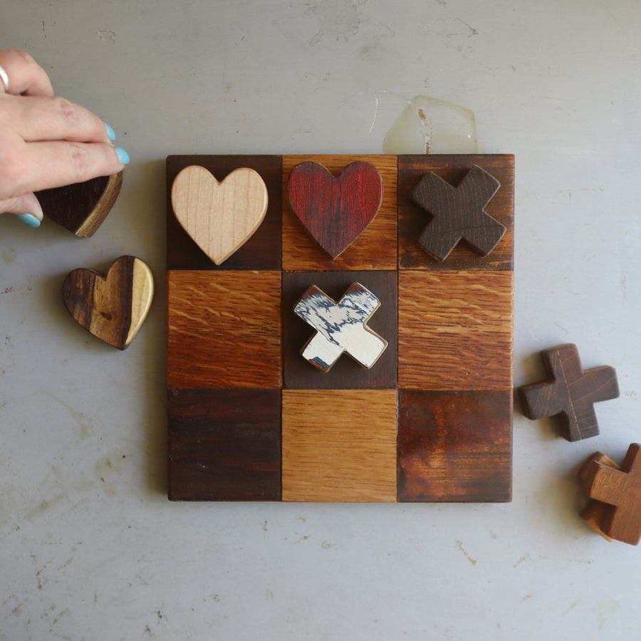 Wooden tic-tac-toe board with heart and X playing pieces.