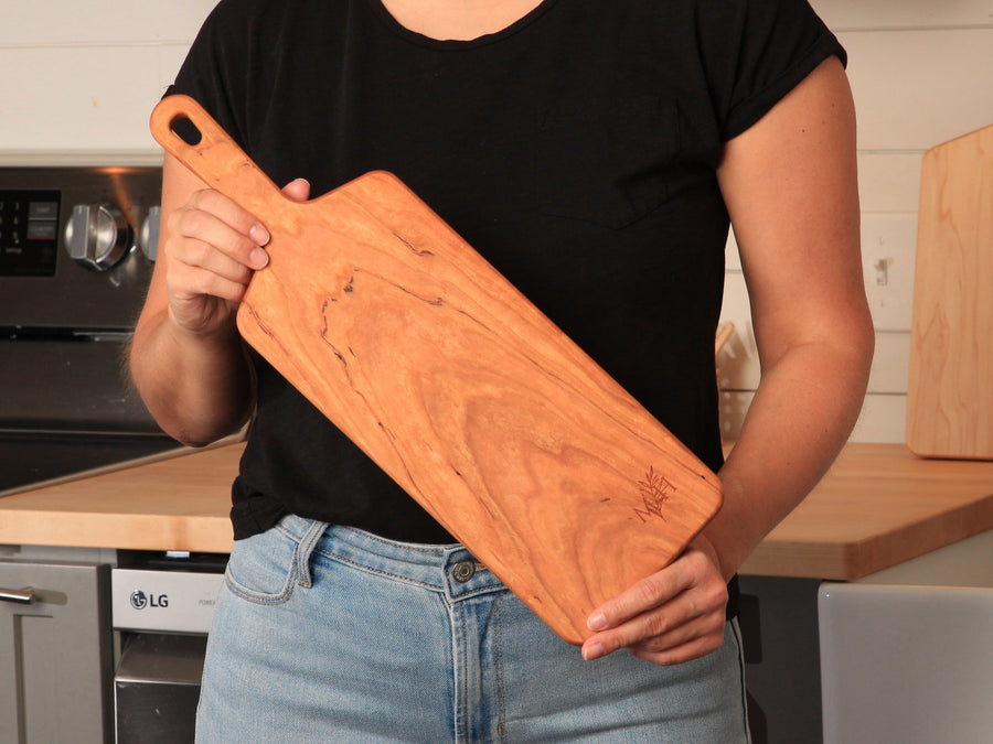 Person holding a narrow cherry paddle serving board