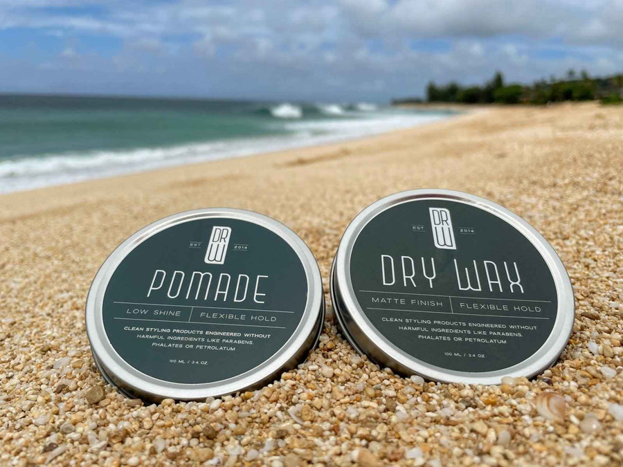 Pomade and Dry Wax jars photographed on a beach