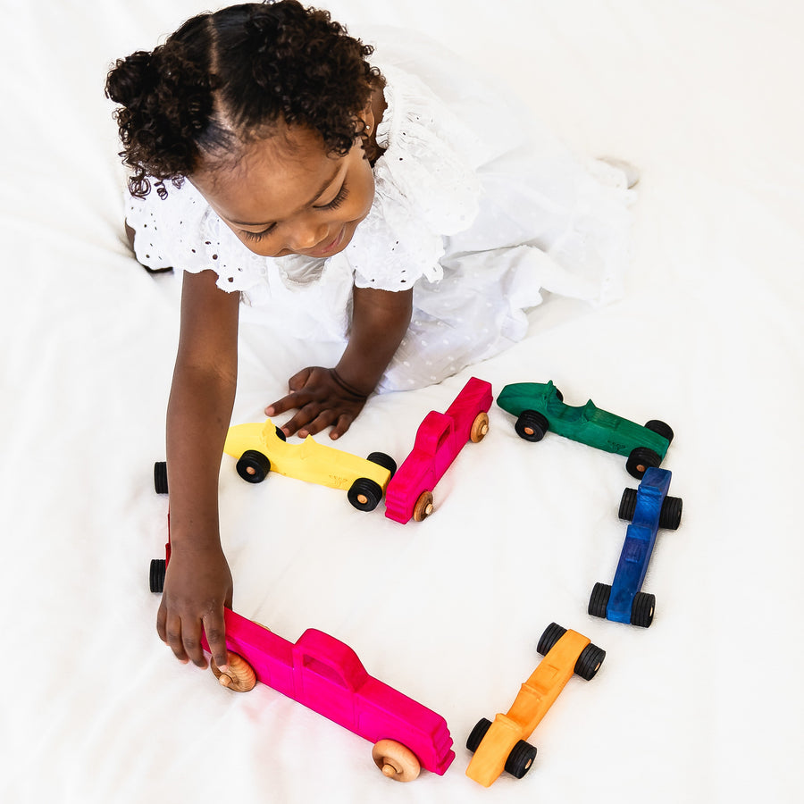 Child arranging colorful wooden toy cars and pickup trucks
