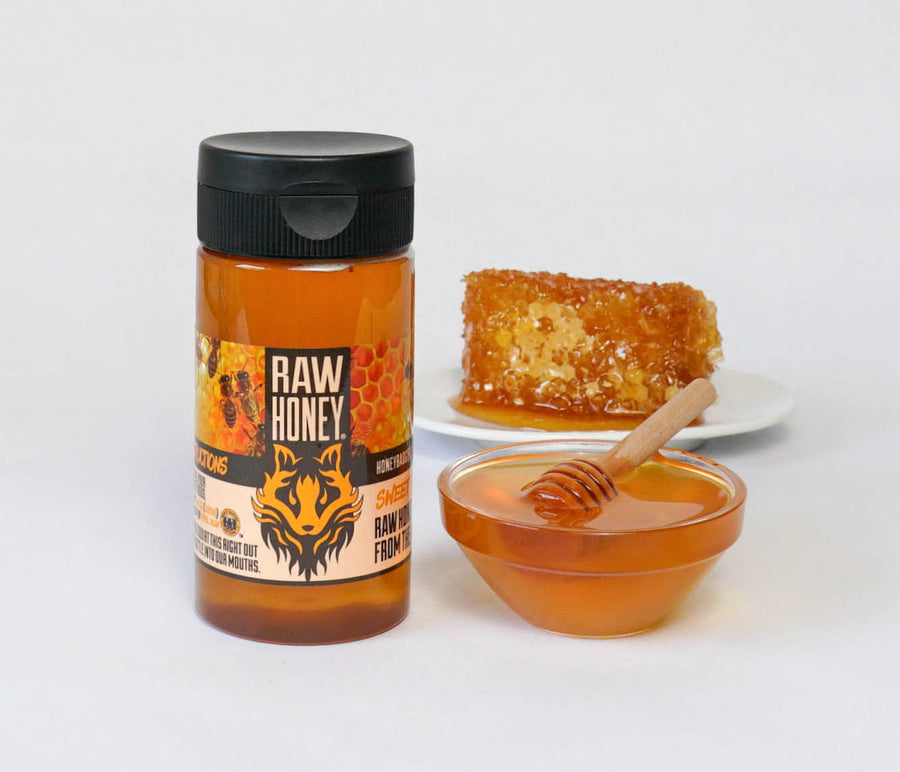 Raw Honey squeeze bottle beside honeycomb and a honey bowl