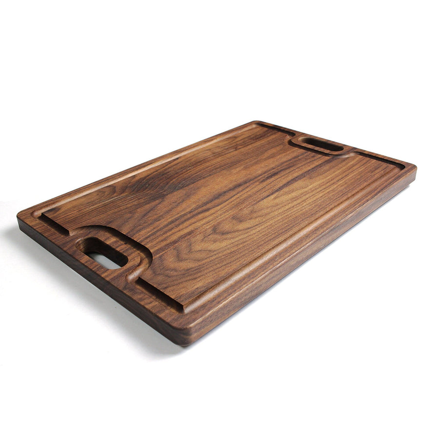 Walnut cutting board with cutout handles and a shaped juice groove, angled view