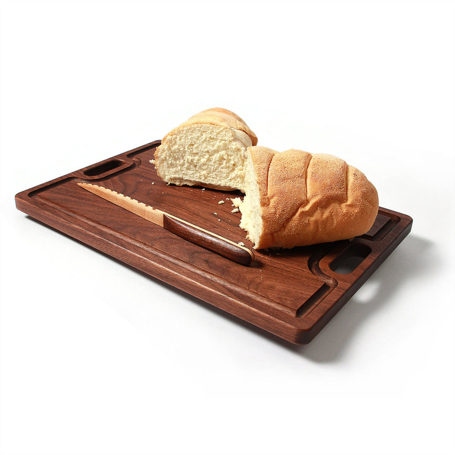 Walnut serving board with cutout handles holding bread and cheese
