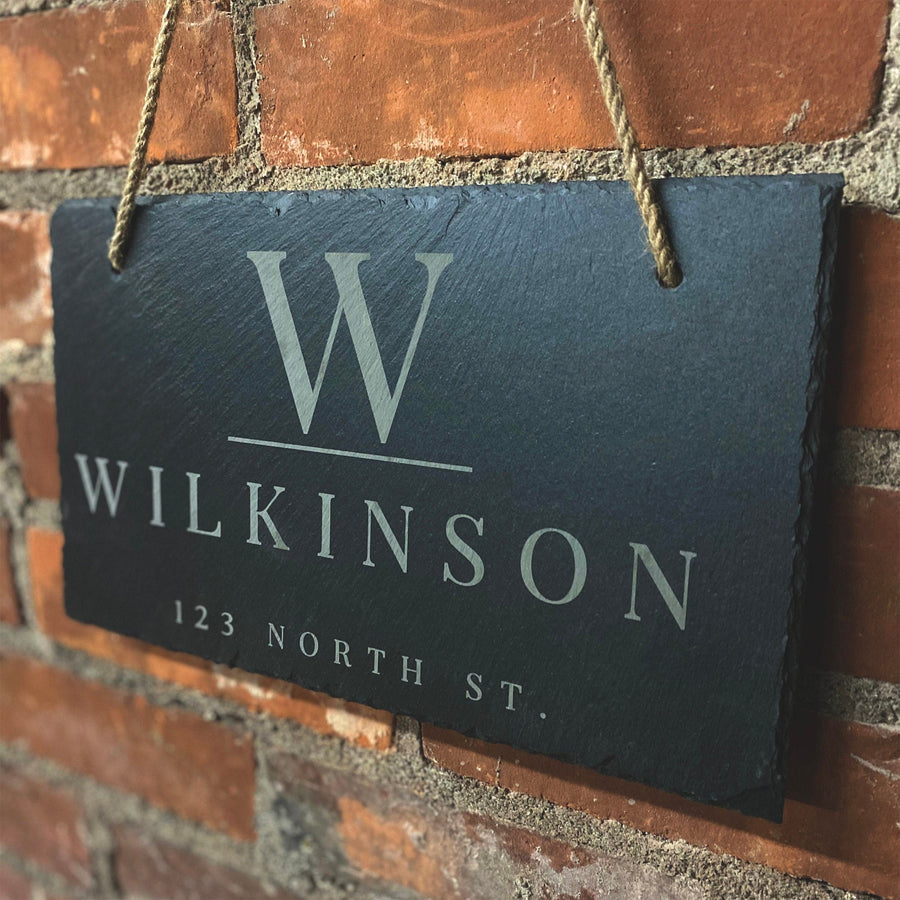 Personalized slate name and address sign hanging from a rope against brick