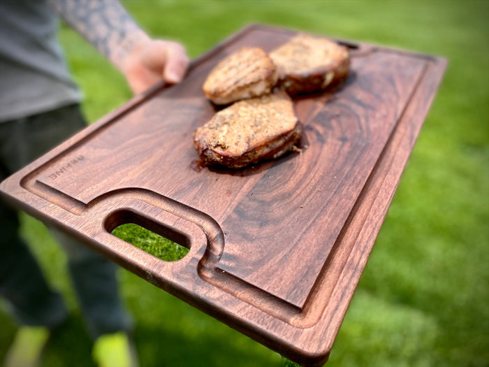 Walnut board with cutout handles being carried with cooked burgers