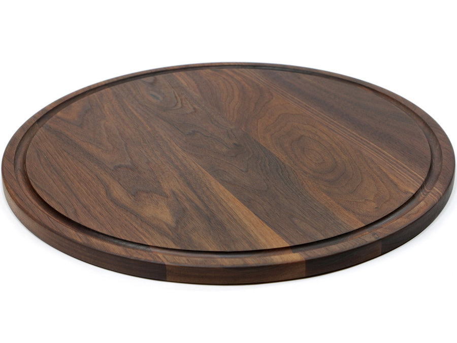 Round walnut board shown at a low angle with its juice groove visible