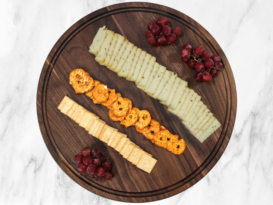 Round walnut serving board arranged with cheese, fruit and appetizers