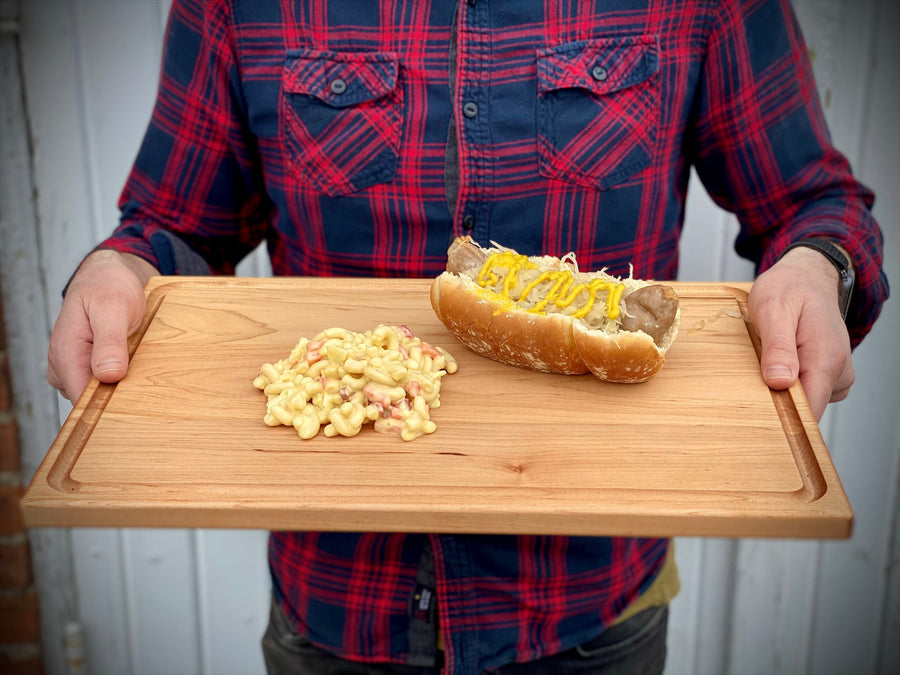 Person holding a maple board with bread, cheese and prepared ingredients