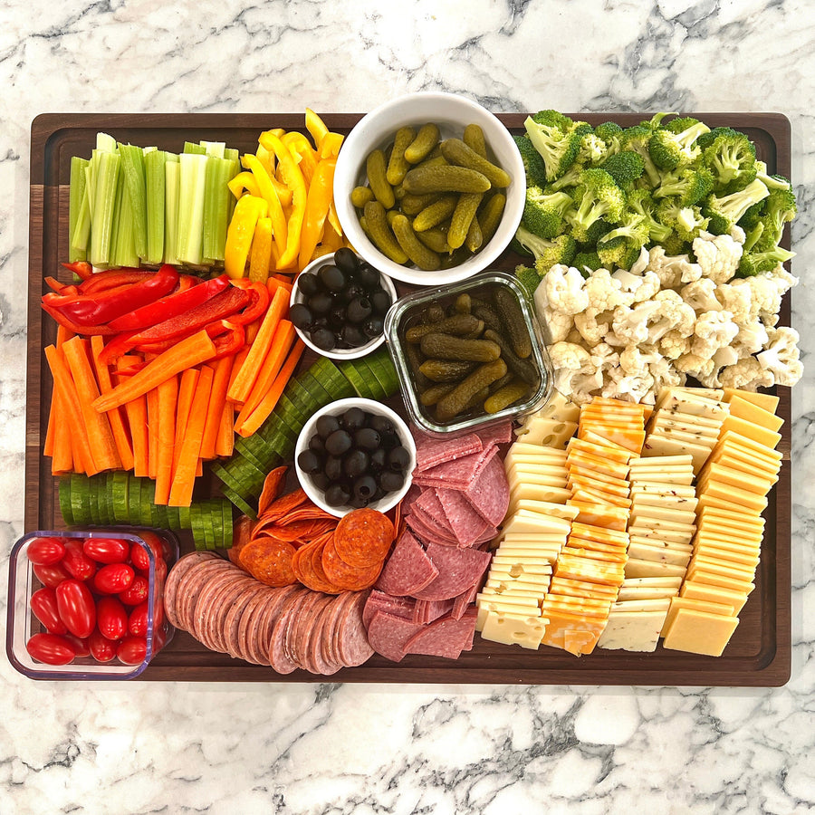 Walnut serving board arranged with vegetables, cheeses and sliced meats