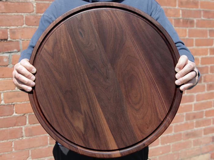 Person holding a round walnut cutting board with a juice groove