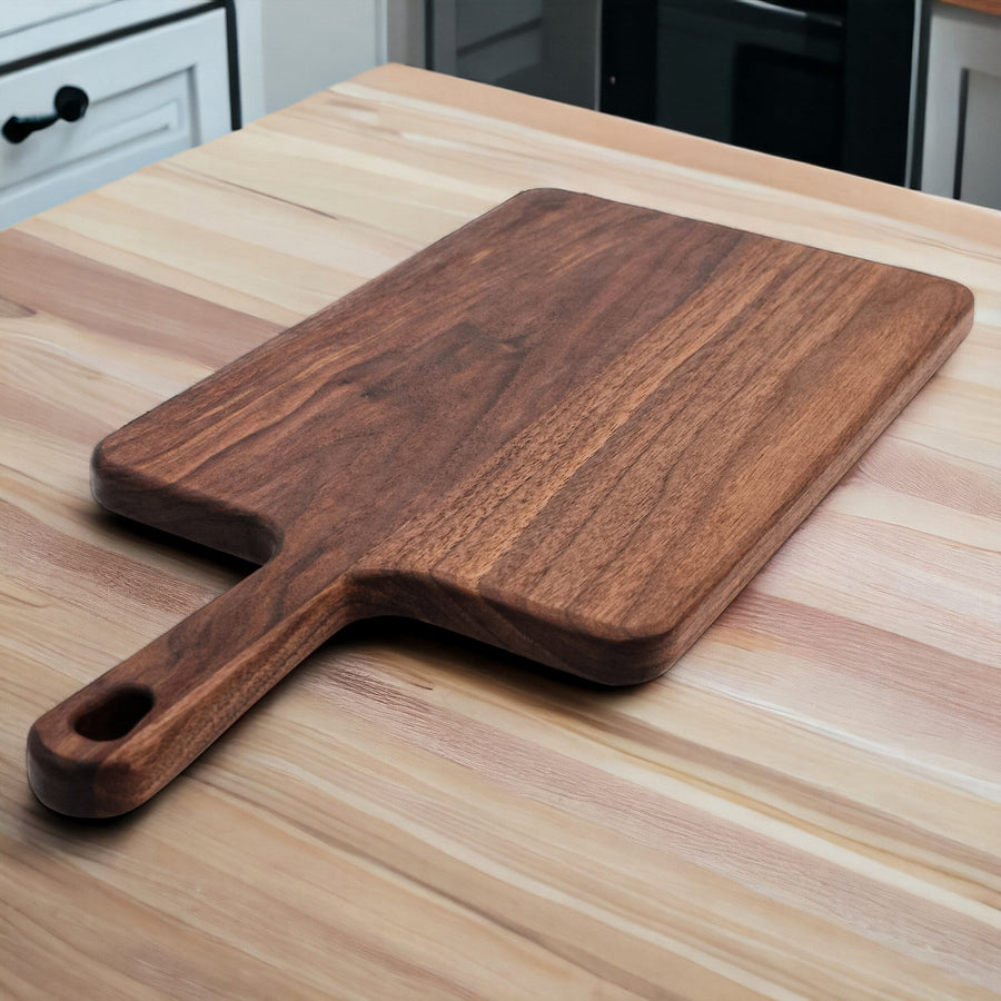 Long walnut paddle serving board resting on a kitchen counter