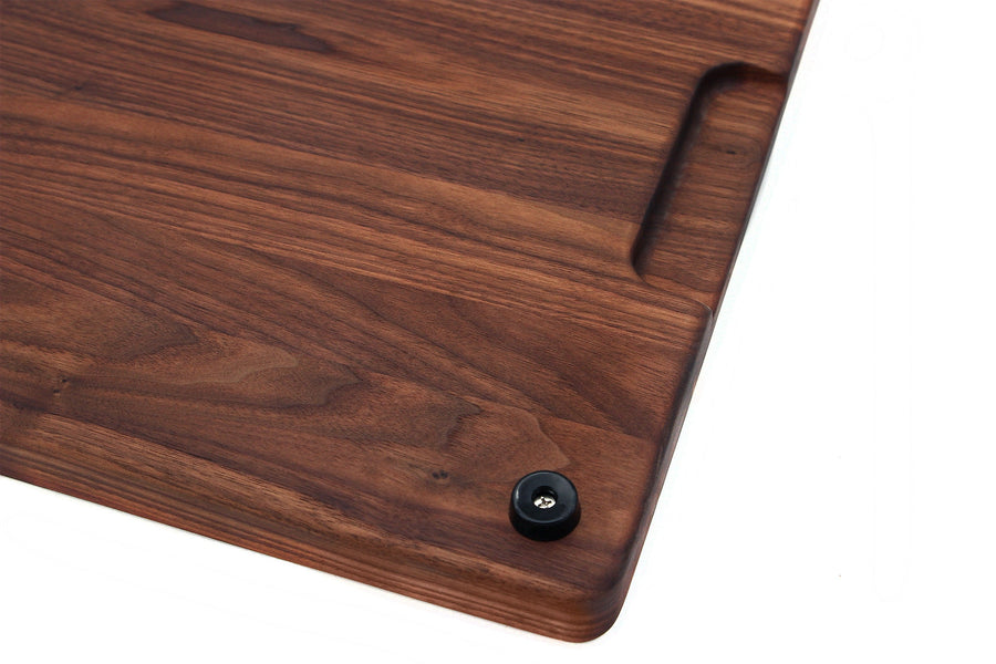 Underside corner of a walnut board showing a rubber foot and pocket handle