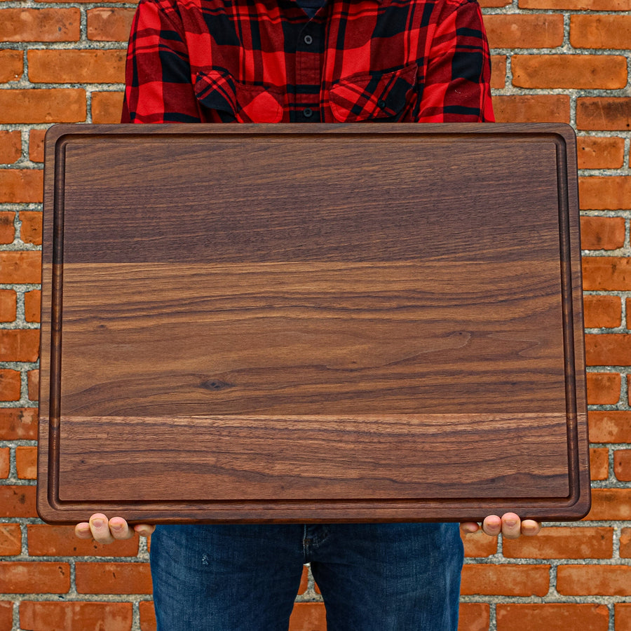 Person holding a large walnut board with a juice groove