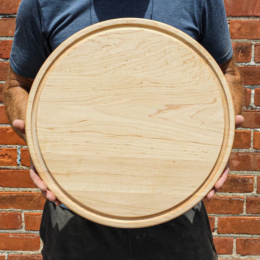 Person holding a round maple cutting board with a perimeter groove