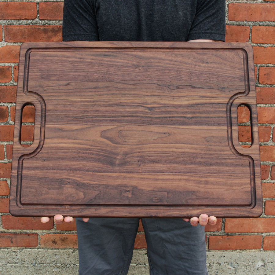 Person holding a large walnut board with a juice groove and cutout handles