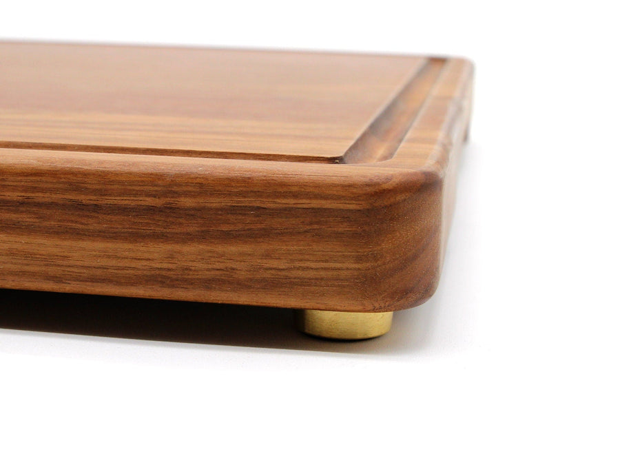 Side view of a wooden cutting board raised on brass feet